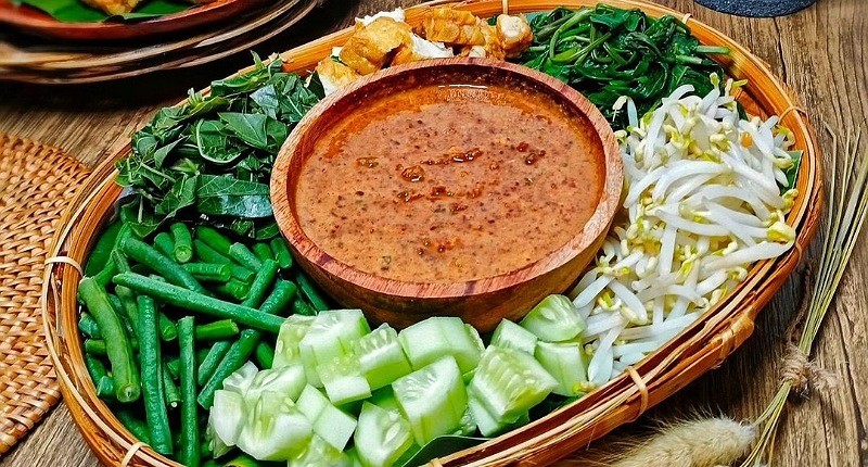 Tampilan dekat pecel sayur dengan bumbu kacang melimpah dan sayuran segar, disajikan dengan rempeyek