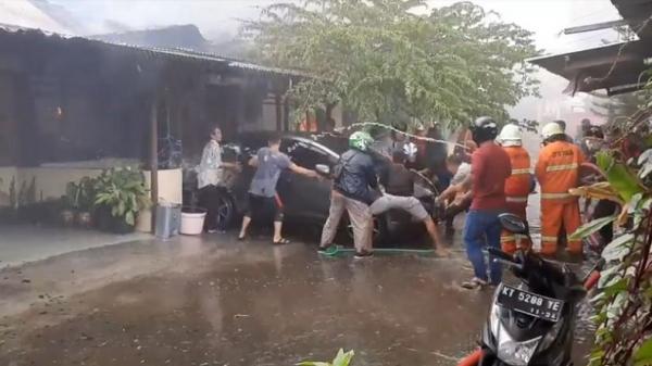 Petugas pemadam dan warga berusaha mendorong mobil menjauh dari rumah yang terbakar di Asrama Polisi Segara di Kota Balikpapan, Kalimantan Timur, Sabtu (11/1/2020). (Foto: iNews/Mukmin Azis)