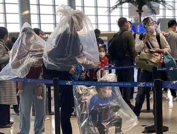 Satu gambar memperlihatkan sebuah keluarga, termasuk seorang ibu menggendong bayinya, mengenakan kantong plastik di bandara. (FOTO: doc.Twitter)