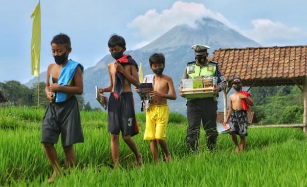 Anggota Polres Mojokerto Aiptu Eriyantono berjalan mengantarkan buku bacaan untuk anak-anak di swah. (istimewa).