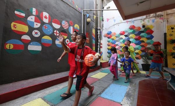 Anak-anak di Surabaya melintasi mural bendera peserta piala dunia U-17. (istimewa).