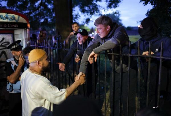 Seorang jemaah Masjid Abdullah Quilliam berjabat tangan dengan seorang pengunjuk rasa selama demonstrasi di masjid yang terletak di Liverpool, Inggris itu, 2 Agustus 2024. (Foto: EPA)