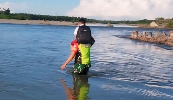 Babinsa Posramil 12/Ptr Kodim 0105/Abar Serka Zulfan memanggul pelajar SD Negeri Meunuang Kinco menyeberangi Sungai Aceh Barat. (Foto Dispenad).