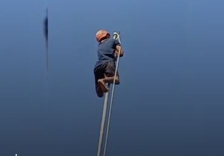 Anggota BPBD Lumajang dengan berani memanjat tiang bendera 15 meter tanpa alat pengaman. (Foto: iNews)